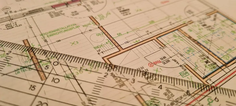 Technische Grundrisszeichnung mit grünen Notizen und transparentem Lineal im Vordergrund, warmes Licht